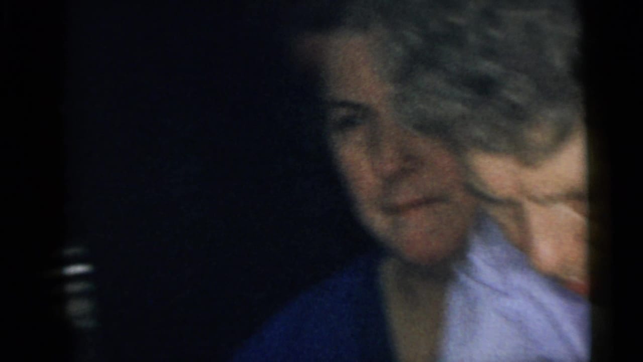 1960 Camden home-movie frame showing two women seated in low light, with one face partly hidden by a person near the lens.