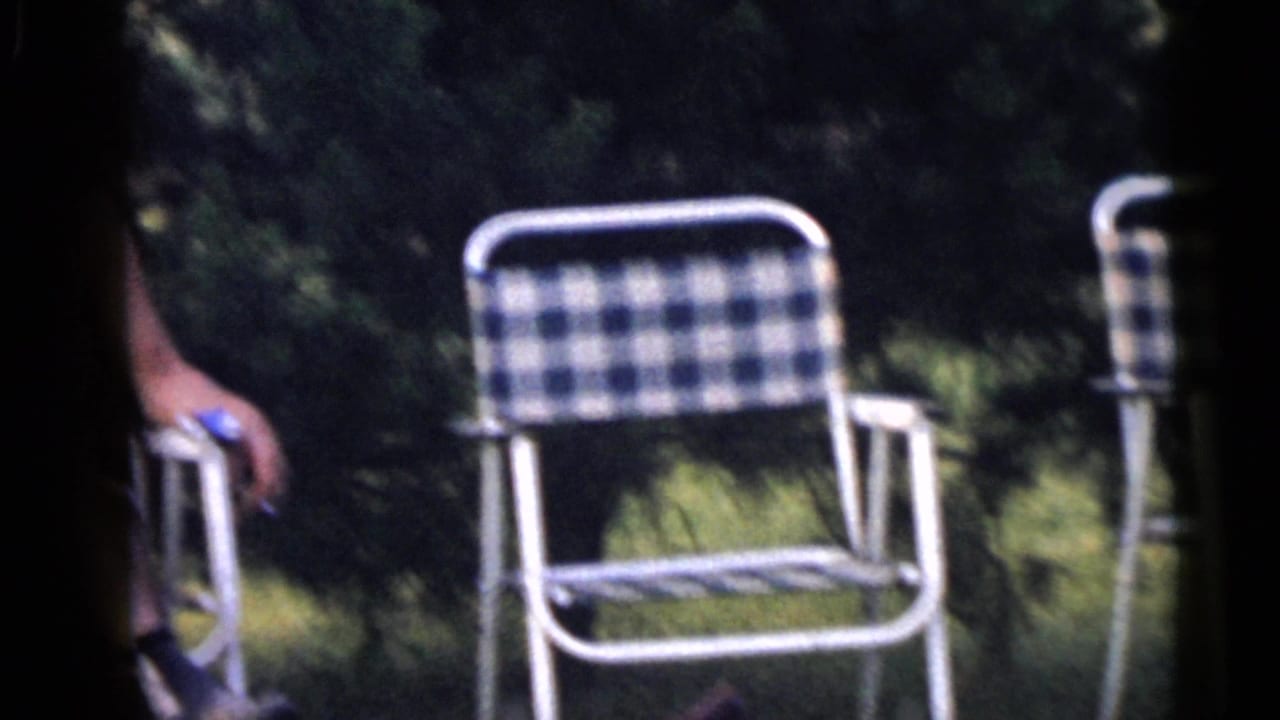 A blue-and-white checkered lawn chair sits on grass in the Camden outdoor scene, with part of a seated person visible at left.