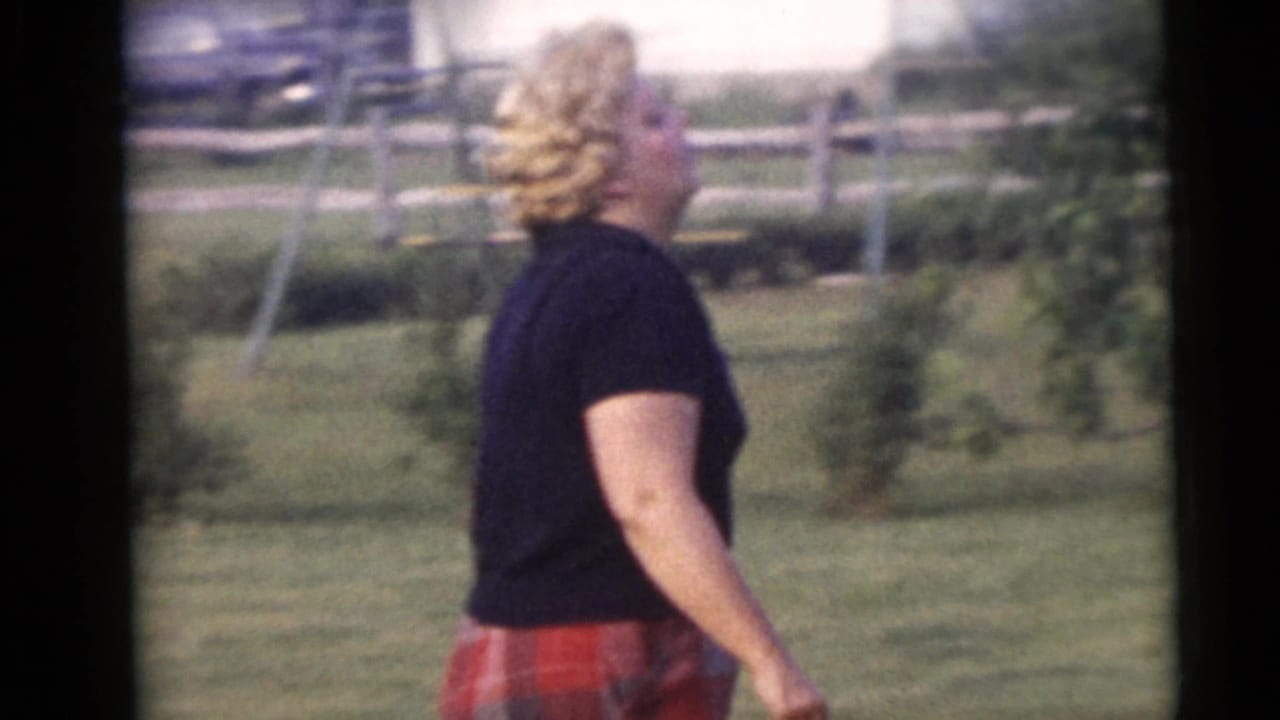 Woman in black shirt and red plaid pants walking across a grassy yard.