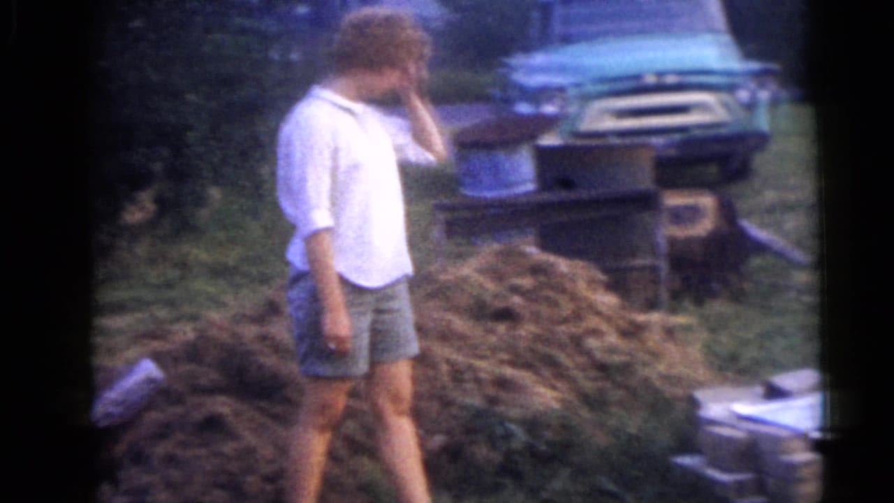 The woman turns near yard debris in the Camden, New Jersey yard, with a teal vintage car and metal containers visible behind her.