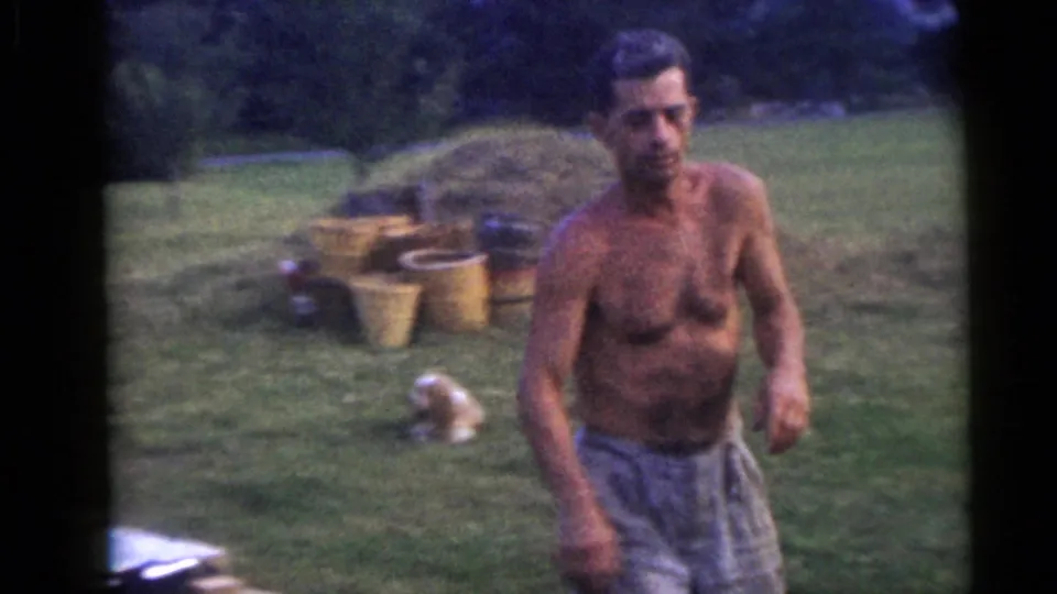 A shirtless man walks across the grassy Camden yard, with buckets, a branch pile, and open lawn visible in the soft 8mm frame.