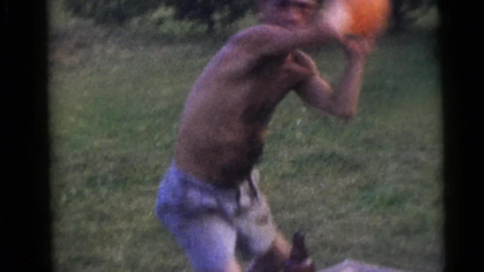 The shirtless man throws an orange ball across the lawn in the 1960 Camden, New Jersey home-movie scene.