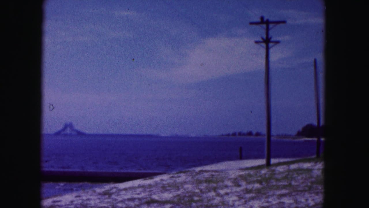 1960 Miami-area coastal view with utility poles along a sandy beach, calm ocean, and a distant landform or structure across the water.