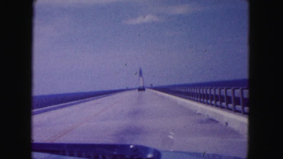 1960 Miami-area 8mm frame from a car on a long bridge over water, looking toward a distant tower.