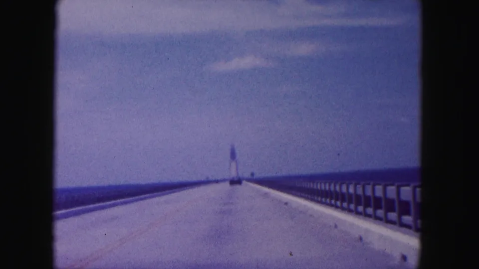 1960 Miami-area bridge view over open water, with railings converging toward a distant lighthouse-like tower.