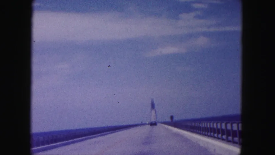 Soft 8mm frame of a 1960 Miami bridge crossing, with water horizon, railings, and a tower-like form in the distance.