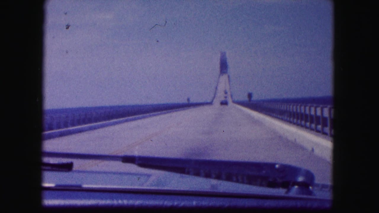 Car hood and windshield edge visible while driving across a bridge toward a distant tower.