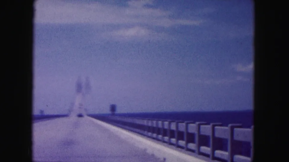 Blurred 1960 Miami-area 8mm home-movie view from a moving car on a bridge, with railings and water visible on both sides.