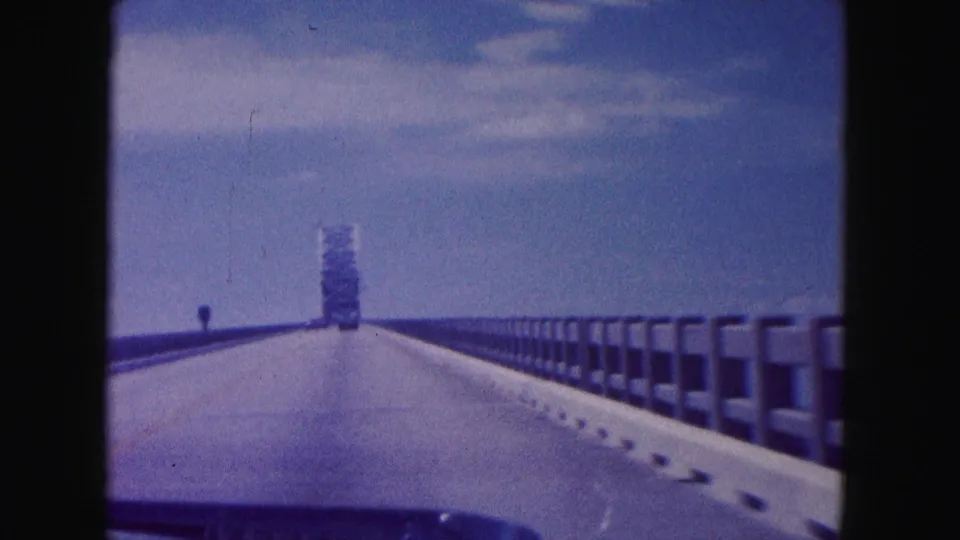 1960 Miami-area 8mm view from a moving car crossing a long elevated bridge toward a distant tower-like structure.