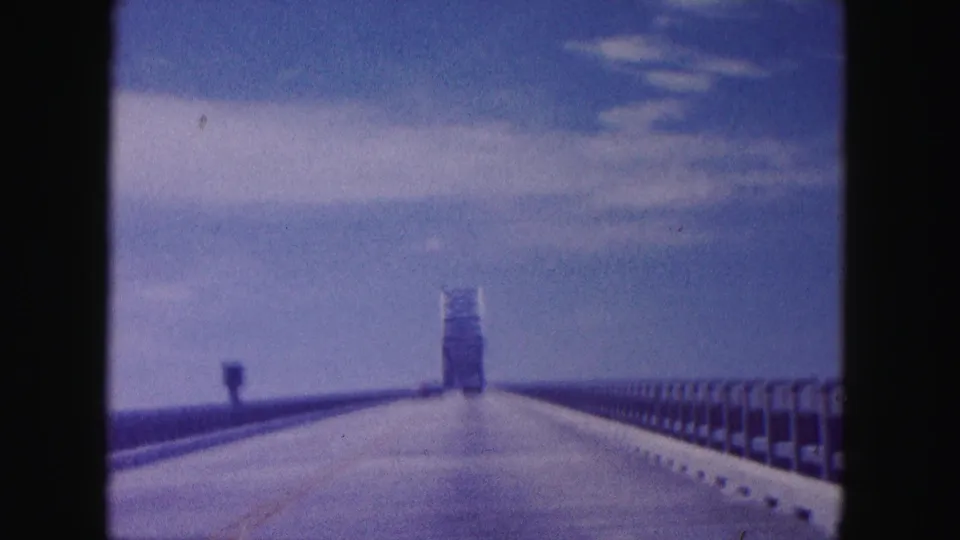 1960s 8mm travel view along a Miami-area bridge, showing open roadway, railings, sky, and the bridge structure ahead.