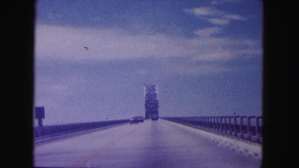 Miami-area 8mm frame showing a car crossing a long bridge with a tower ahead and a few vehicles visible on the road.