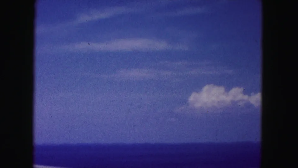 1960 Miami-area home-movie frame showing water, hazy sky, and clouds through a dark moving-car window edge.