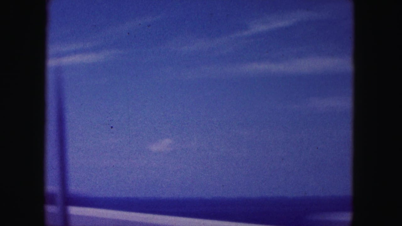 Water horizon and blue sky framed by dark vertical window edges.