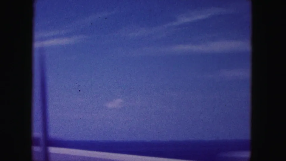 Blue-tinted 1960 Miami-area travel view of open water and sky from a moving car window.