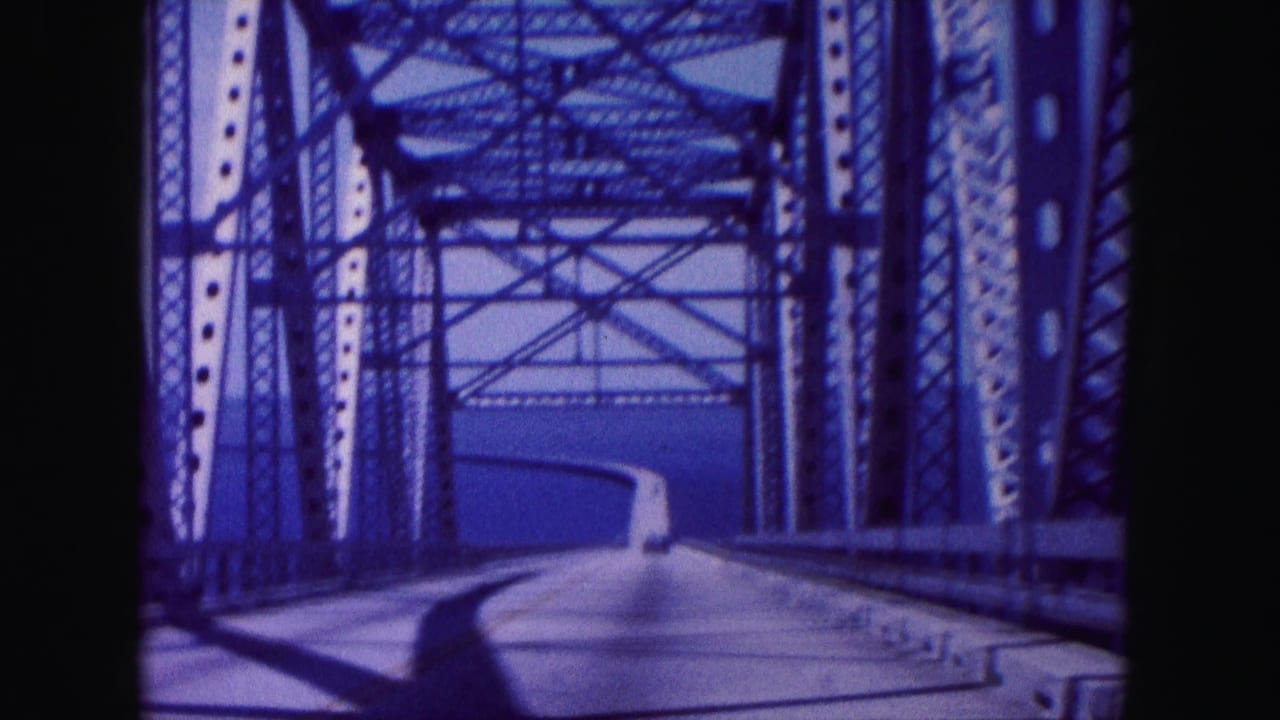 Bridge roadway seen through steel beams with water in the distance.