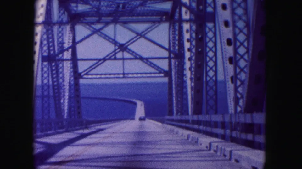 8mm home-movie frame of a 1960 bridge crossing near Miami, with metal bracing, road shadows, and water ahead.
