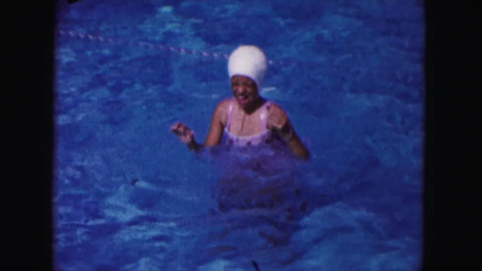 1960 Miami home-movie frame of a swimmer in a white cap and swimsuit facing the camera from inside the pool.