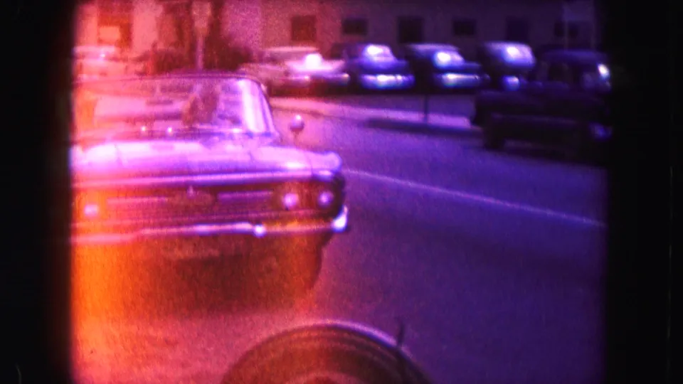 1960 Miami 8mm frame of a classic convertible approaching on a nighttime street with parked cars along the curb.
