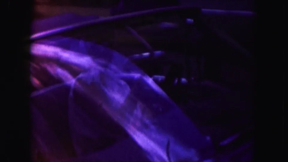 Dim 8mm view into the convertible interior, with a partly visible occupant and upholstery under strong purple-blue color shift.