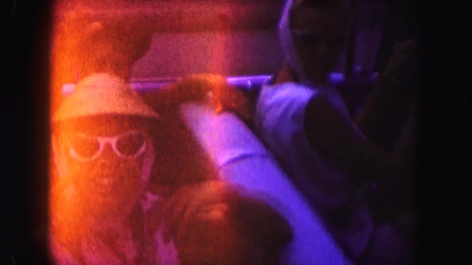 In this 1960 Miami home-movie frame, a woman wearing sunglasses sits in an open convertible under heavy orange-purple film flare.