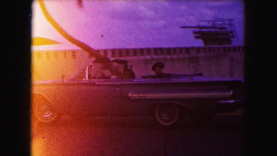 1960 Miami 8mm frame showing a classic convertible beside a roadside hotel-motel sign, with strong light leak and grain.