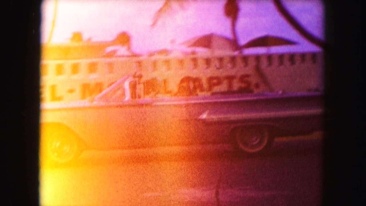 Convertible in front of a hotel-motel building, partly obscured by bright film flare.