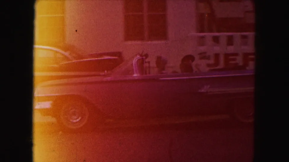 1960 Miami home-movie frame showing a classic convertible passing hotel-motel signage with tinted grain and frame shadow.