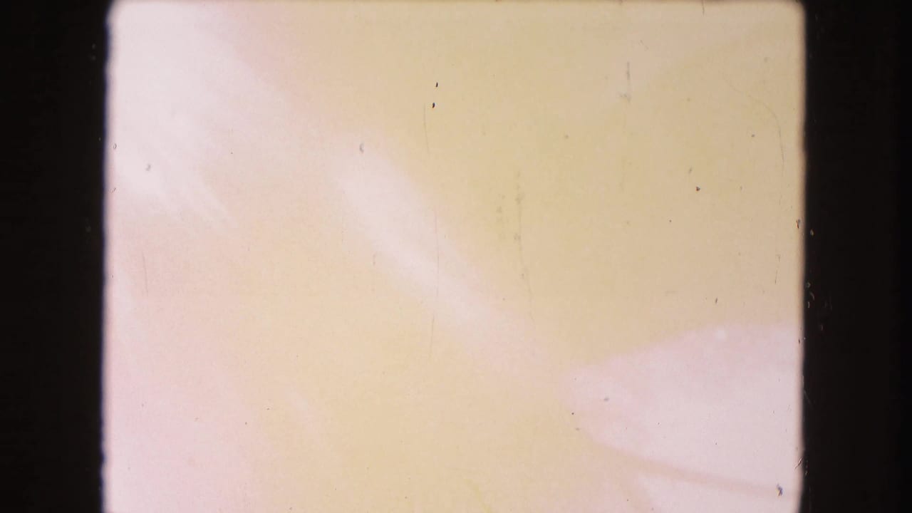 Pale overexposed film frame with soft yellow and pink color wash and black gate borders.