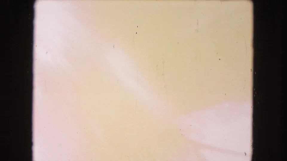 1960 Miami 8mm frame with a pale yellow-pink wash, visible film border, dust specks, and no identifiable subject yet.