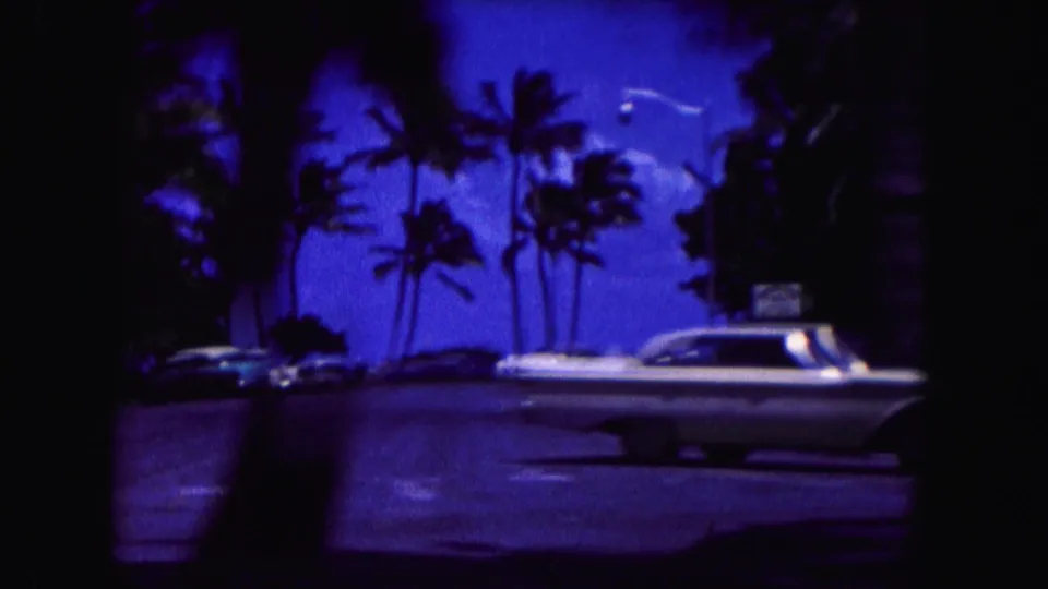 1960 Miami roadside view with a white classic car, palms, parked cars, and deep blue film color shift.