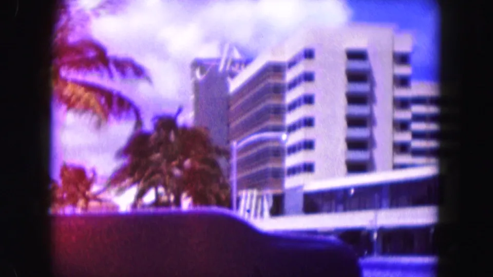 1960 Miami view of a mid-century apartment or hotel building framed by palms, wall, and vivid 8mm color.