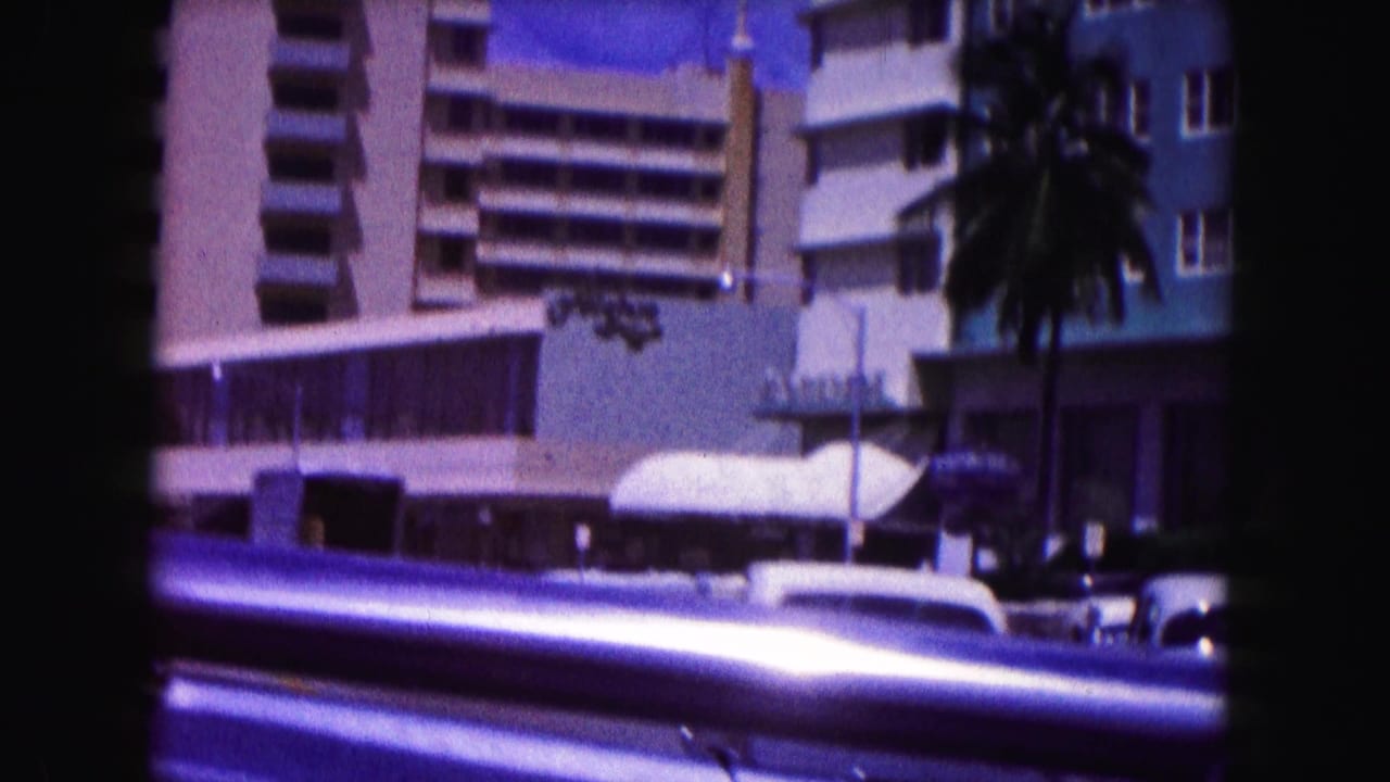Hotel facade with balconies and a blurred car passing in front.