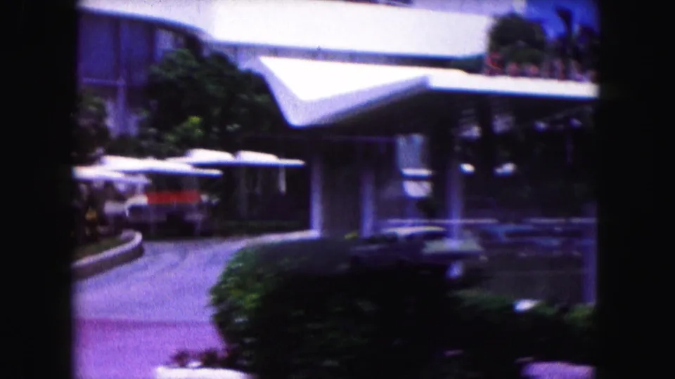1960 Miami home-movie view of a curved drive, white canopy, palms, and classic cars near a modern building.