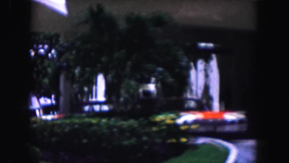 1960 Miami frame with palms, hedges, a white classic car, and a shaded modern building entrance.