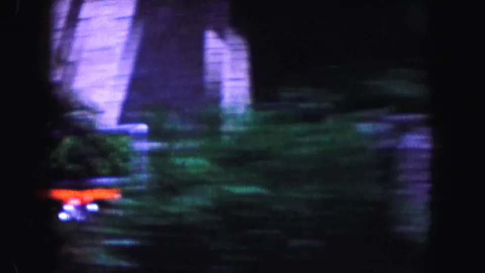 Motion-blurred 1960 Miami street view with a residential exterior, dense greenery, and a passing or parked car detail.