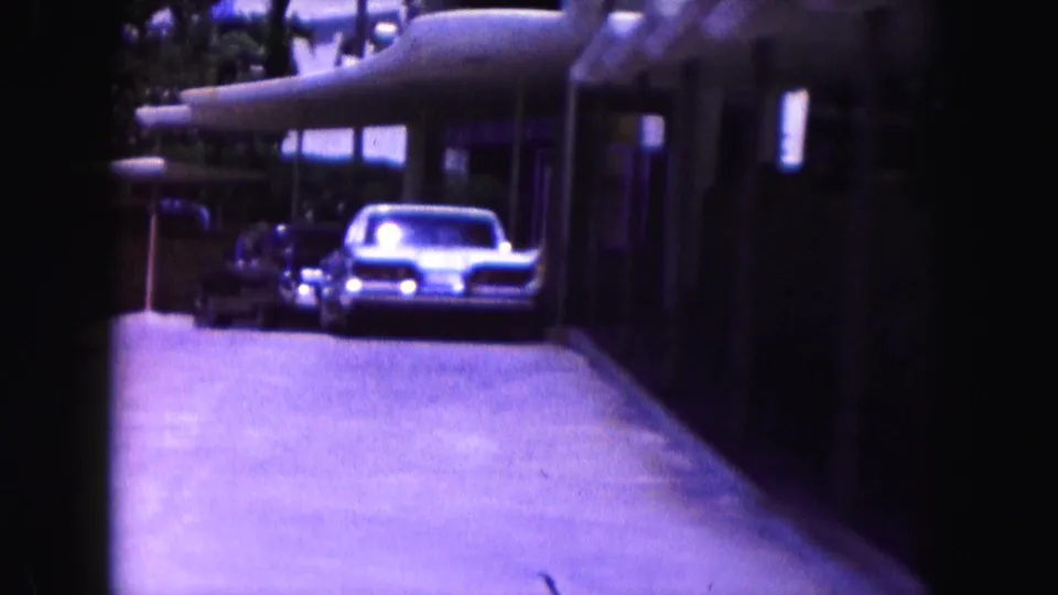 1960 Miami frame showing a driveway or covered entry with parked cars beside a residential or lodging-style building.