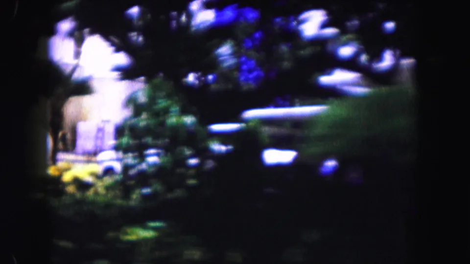Motion-blurred 1960 Miami home-movie view of palms, shrubs, and a parked car along a residential street.