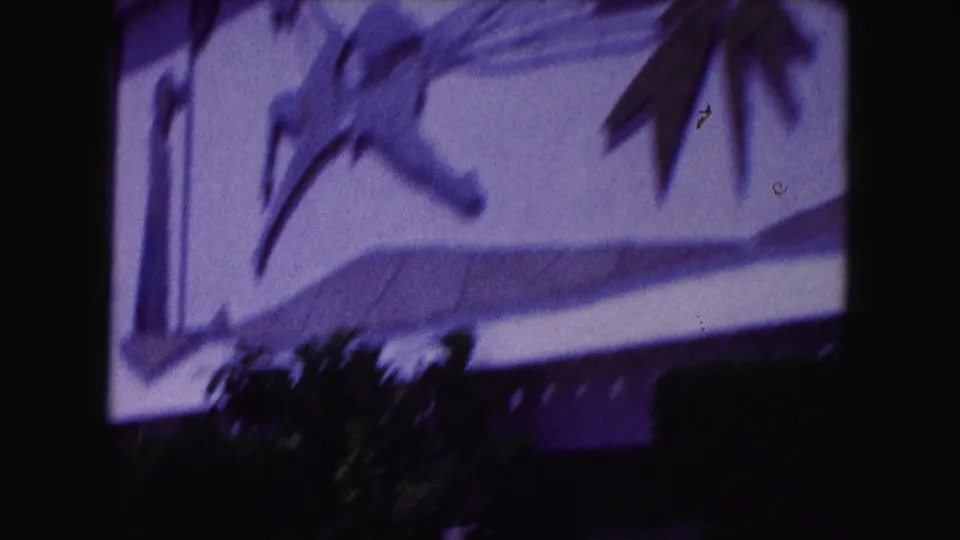 Closer 1960 Miami view of a stylized figure and sweeping decorative shapes on an exterior wall, with foliage at the lower edge.