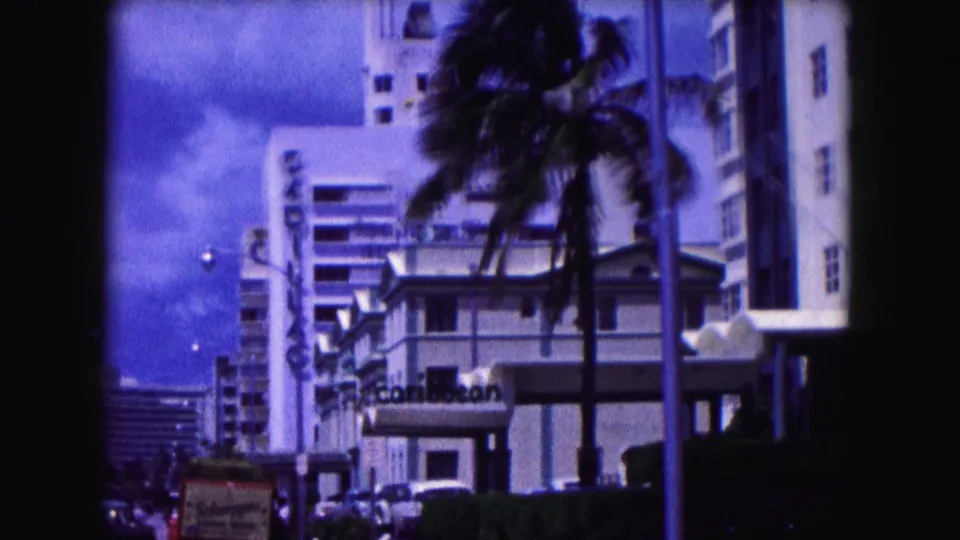 1960 Miami street frame showing palm trees, hotel facades, vertical signage, and parked cars under a bright sky.