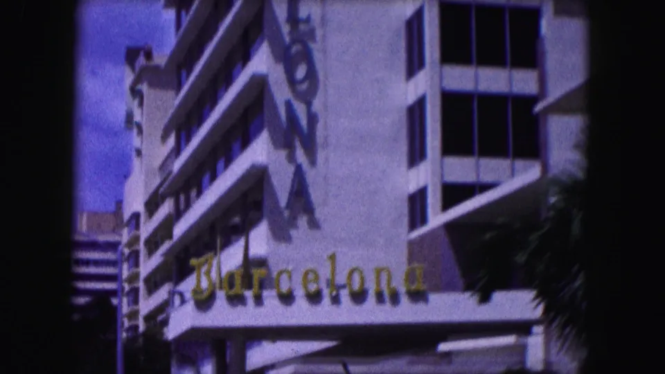 1960 Miami frame showing a hotel-like facade with Barcelona lettering, balconies, windows, and a vertical sign along the building edge.