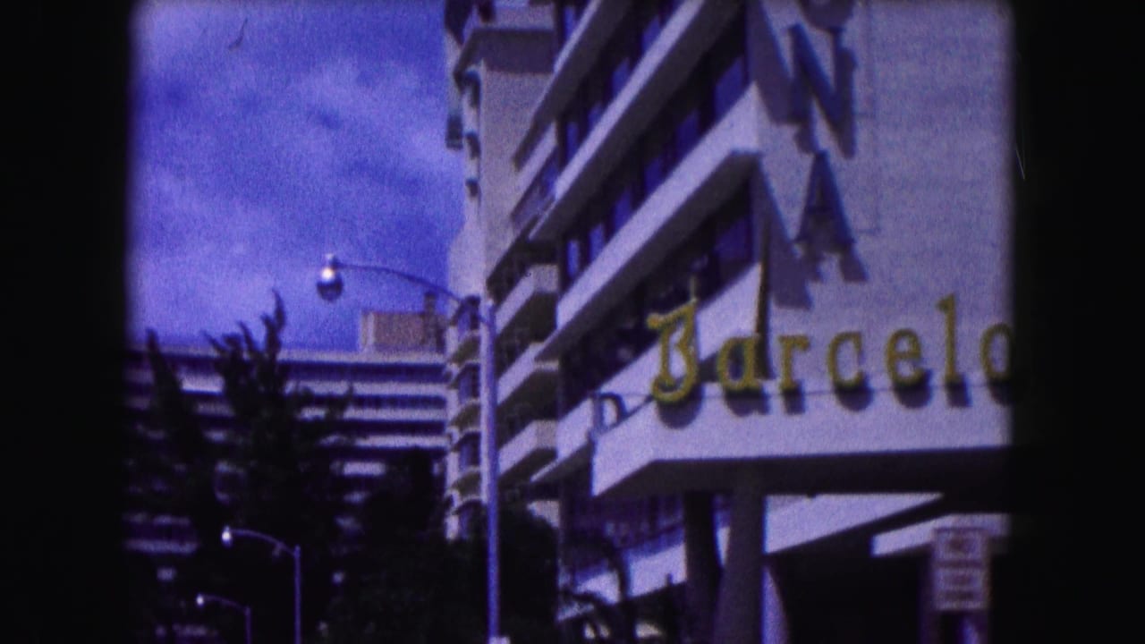 White building with a partial Barcelona sign, palm trees, and a sunny street.