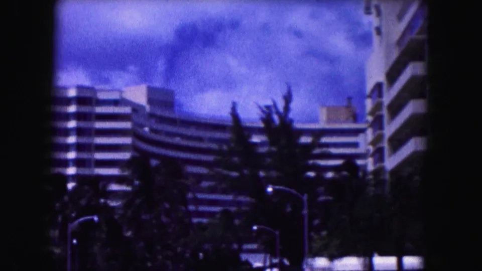 1960 Miami street view showing a curved white modernist building, dark tree line, streetlamp, and saturated blue sky.