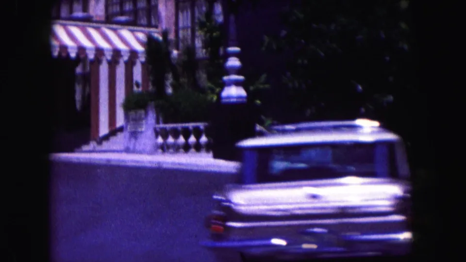 1960 Miami drive-by view of a light-colored classic station wagon beside striped awnings, a balustrade, and street greenery.
