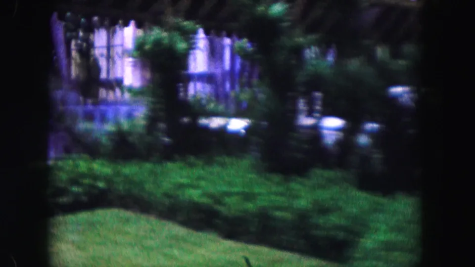 1960 Miami exterior view with trimmed shrubs, lawn, trees, and a building facade partly obscured by garden planting.