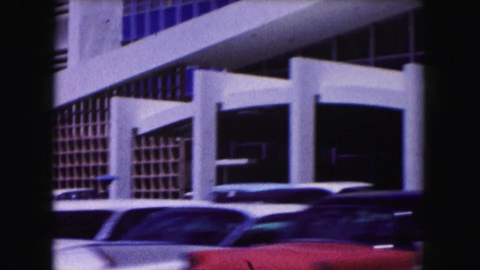 1960 Miami 8mm frame showing white concrete supports, gridded windows, and classic cars in a parking area.