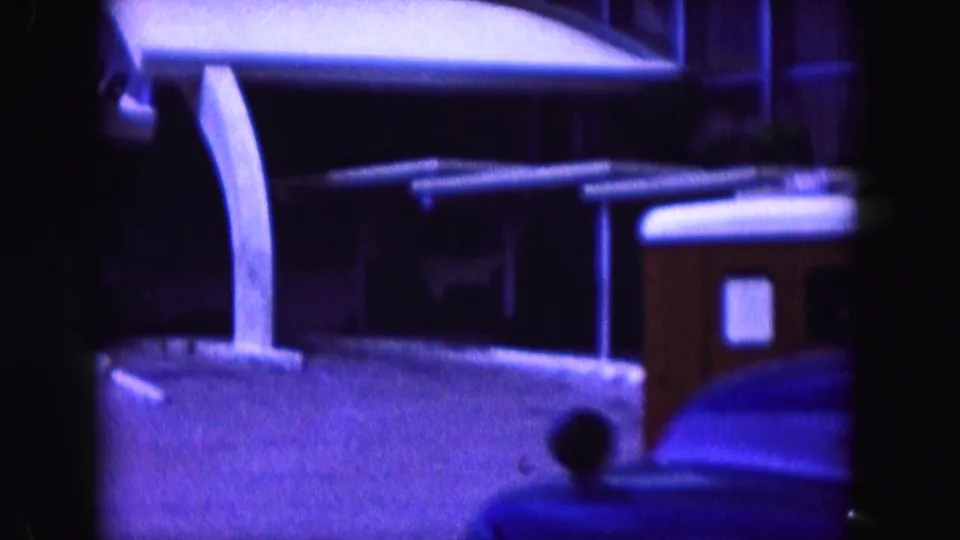 1960 Miami hotel entrance under a white canopy, with driveway paving, structural supports, and a dark indistinct person near the covered area.