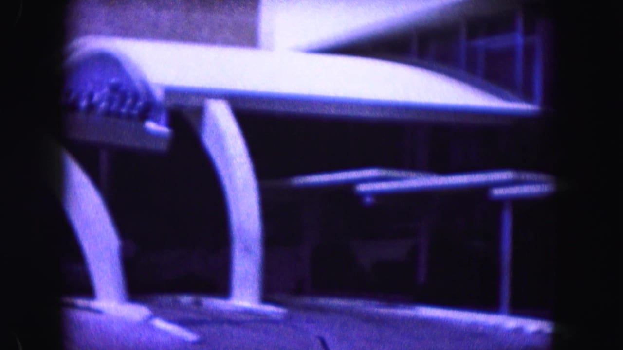 Curved building canopy and dark foreground framing in blue-purple 8mm footage.