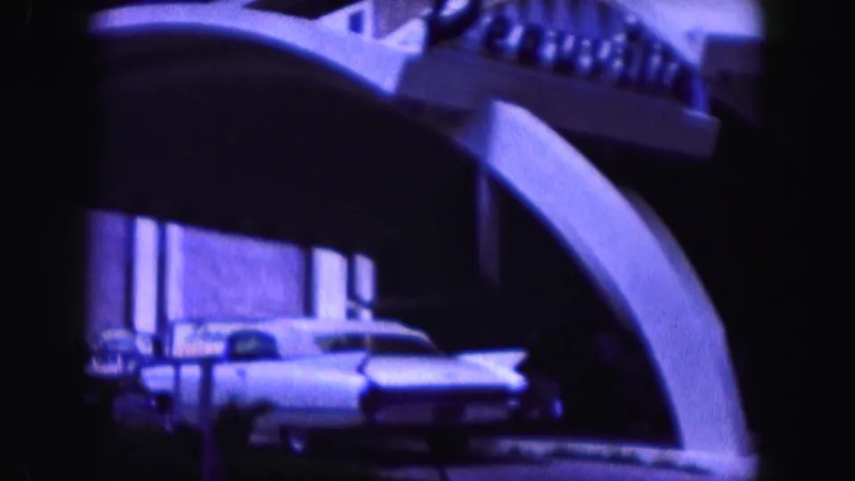 White finned car passes a modern building in the stated 1960 Miami footage, with possible signage visible near the entrance.