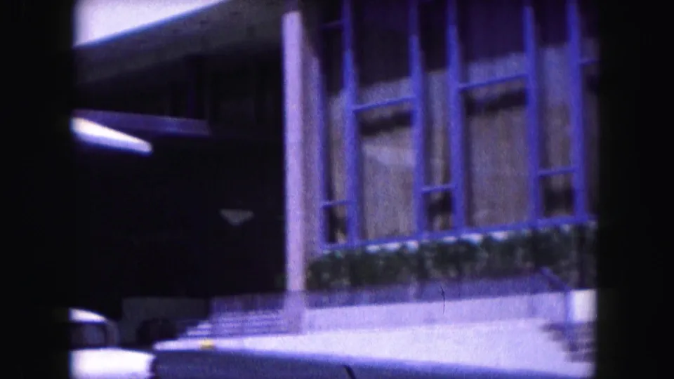 Miami building exterior with steps, tall windows, hedge planting, and curved canopy edge in aged 8mm color footage.