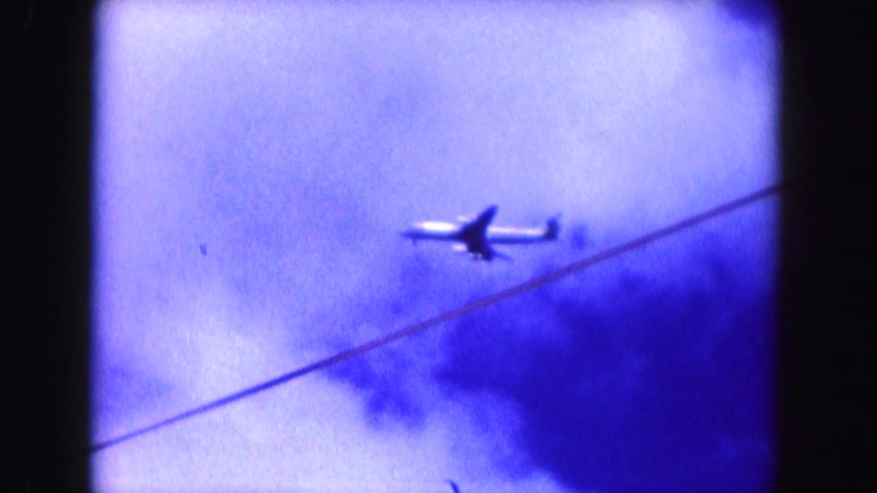 A small commercial airplane appears in the blue-purple Miami sky above a diagonal overhead line in this 1960 8mm frame.